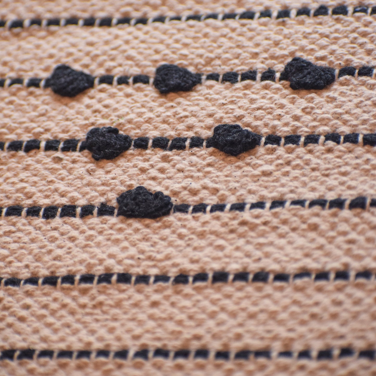 Close-up of woven fabric with black thread pattern on beige background