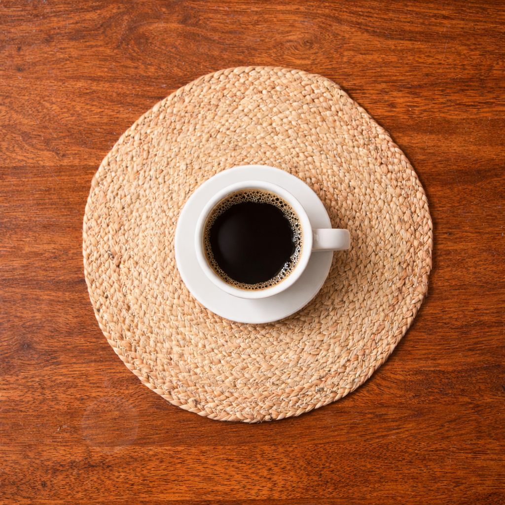 White cup of coffee on a woven placemat with a wooden table background