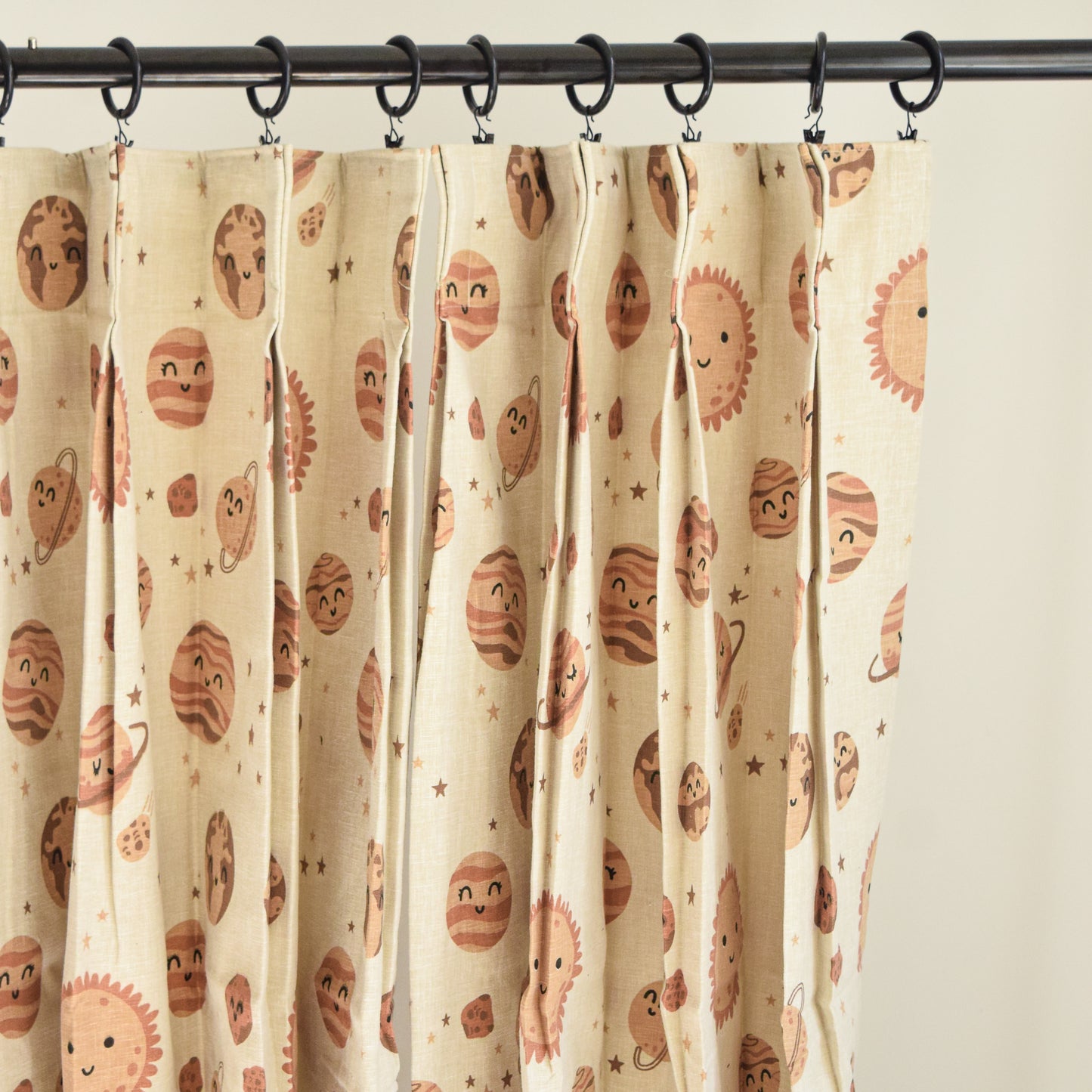 Curtains with a pattern of cartoon-like planets hanging on a rod.