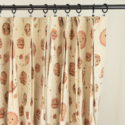 Curtains with a pattern of cartoon-like planets hanging on a rod.