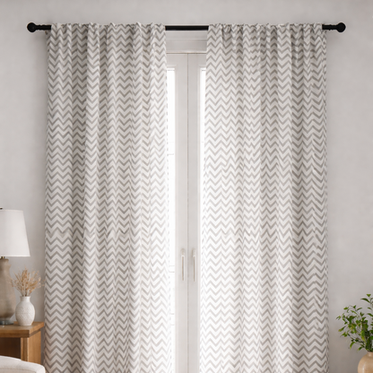 Patterned curtains hanging in a room with a lamp and plant on either side.