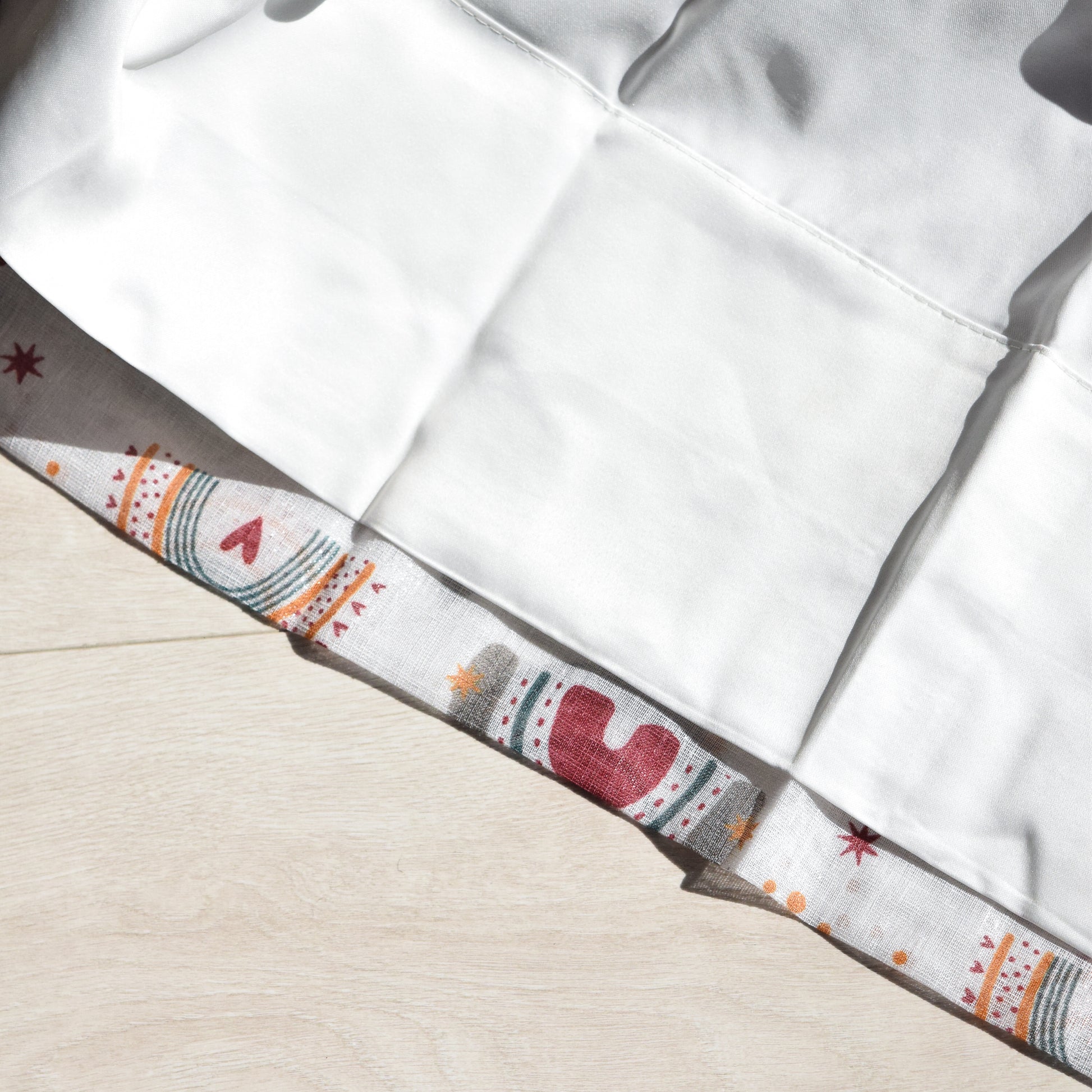 Close-up of a white curtain lining with a patterned trim on a beige background