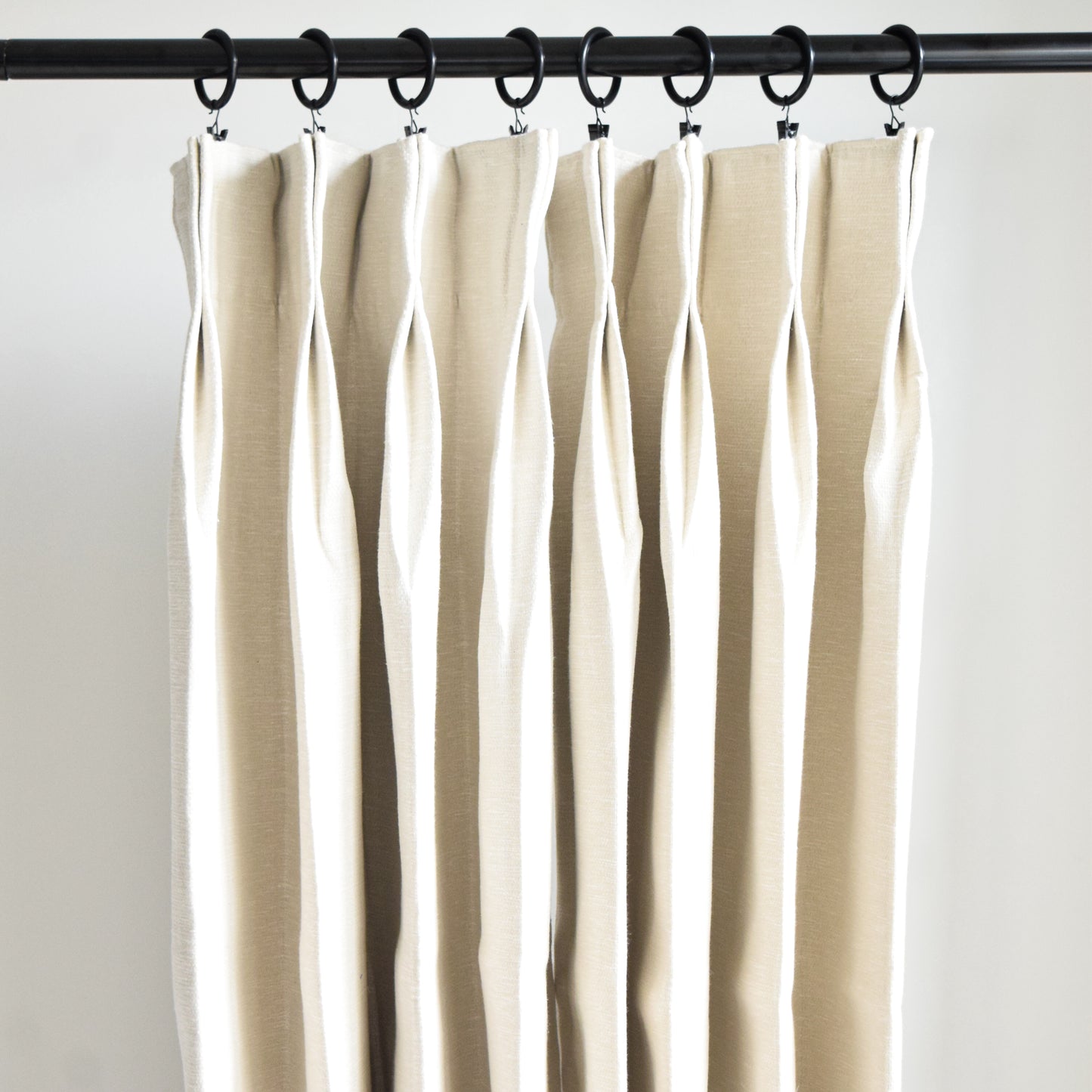 Beige curtains hanging from a rod against a white background