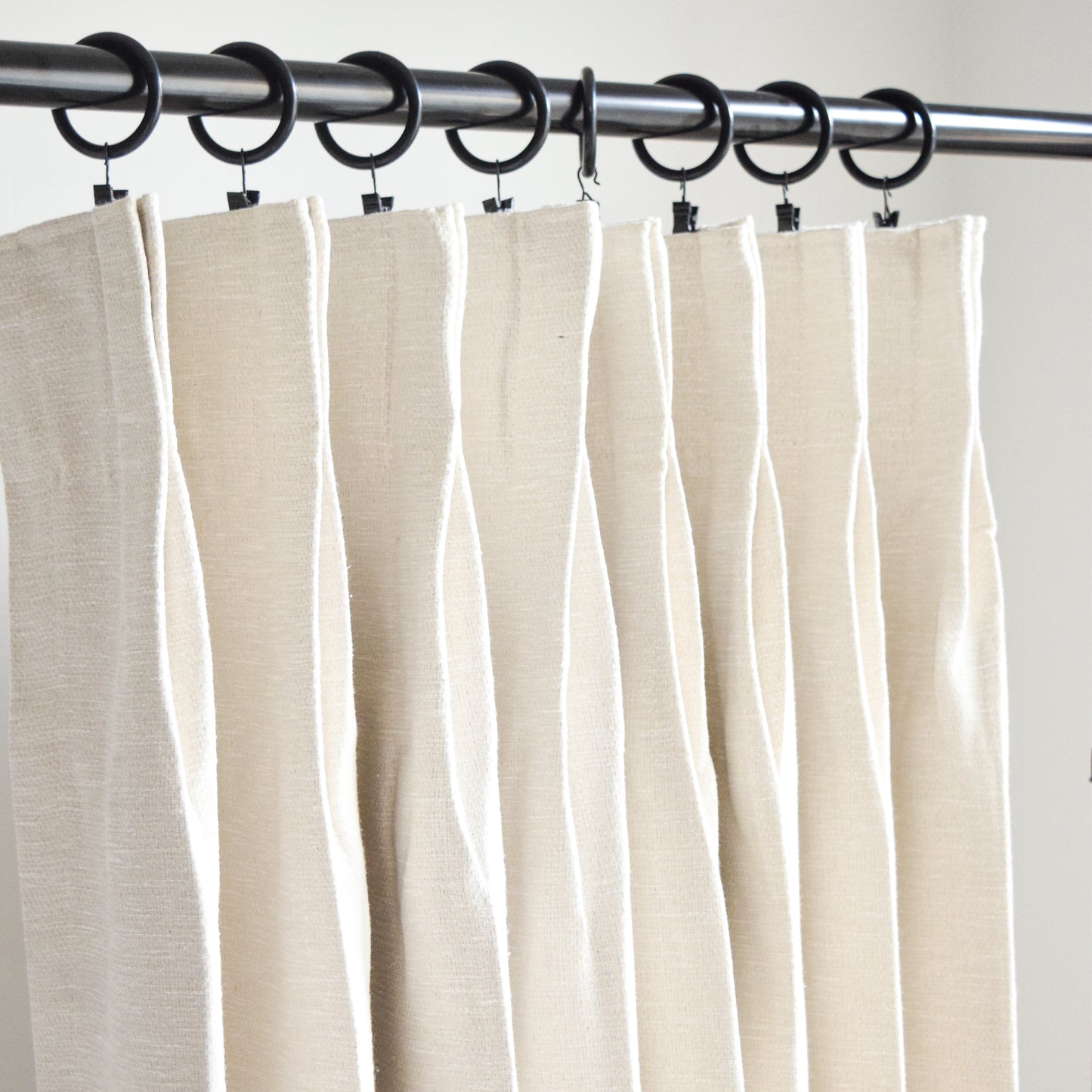 Beige curtains hanging on a rod with clips against a plain background