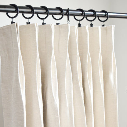 Beige curtains hanging on a rod with clips against a plain background