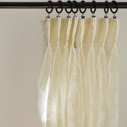 Sheer beige curtain with textured pattern hanging from a rod against a neutral background