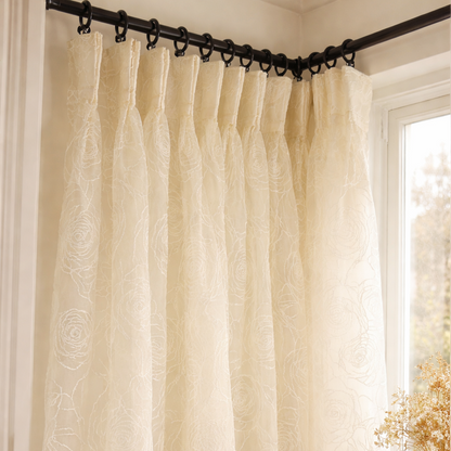 Beige curtain hanging from a rod with a window and table in the background