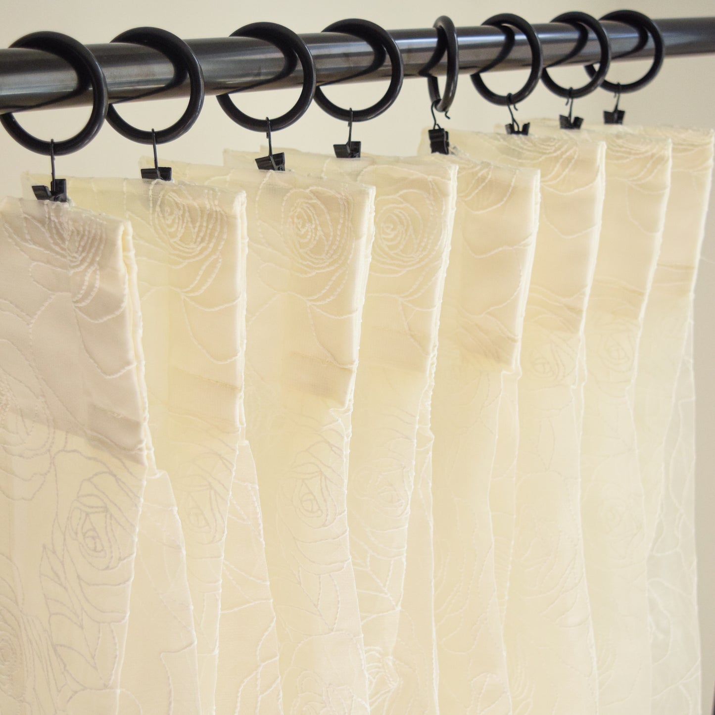 Beige curtains with a textured pattern hanging from a rod with black rings and clips.