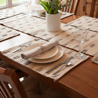 Dining table set with placemats, plates, cutlery, and a vase with flowers.