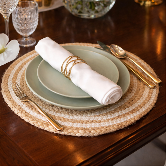 Dining table setting with plates, napkin, and cutlery on a woven placemat.