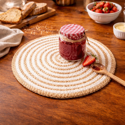 Jar of red jam on a woven placemat with strawberries and bread in the background