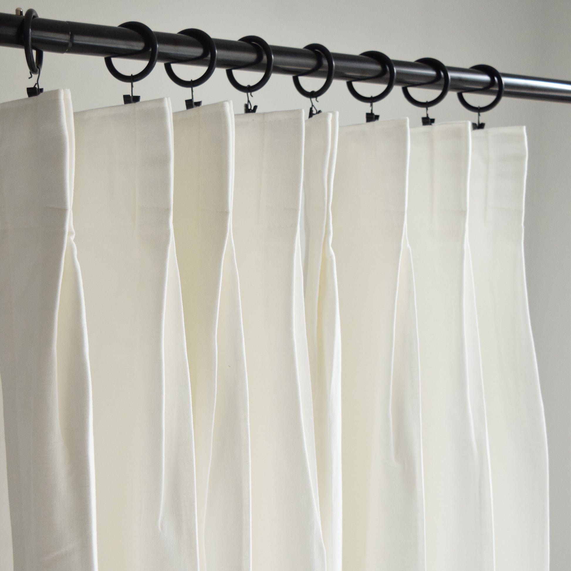 White curtains hanging from a black curtain rod against a neutral background