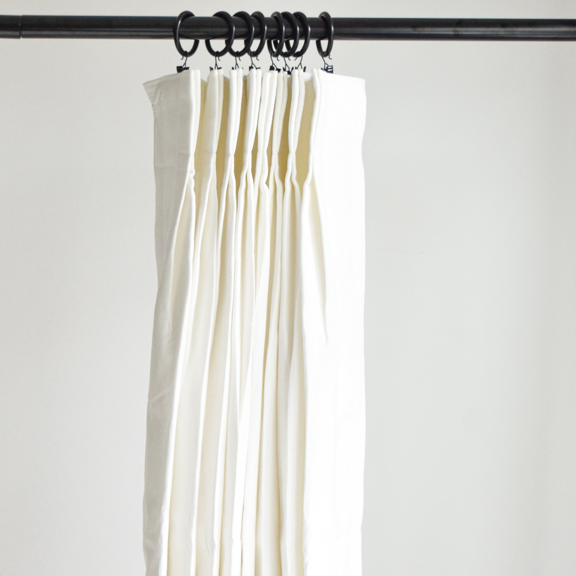 White curtains hanging from a rod against a plain background